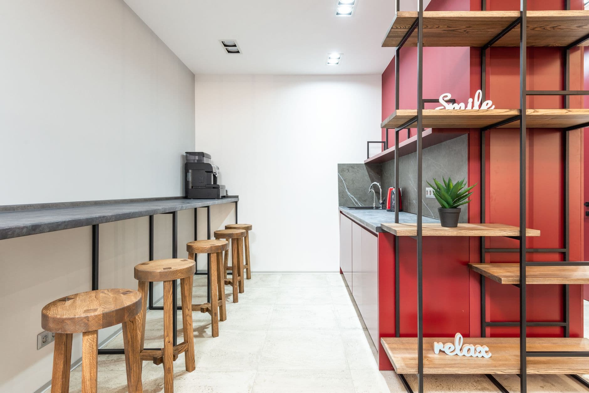 A counter-height work surface with stools beside a kitchen area and open shelving