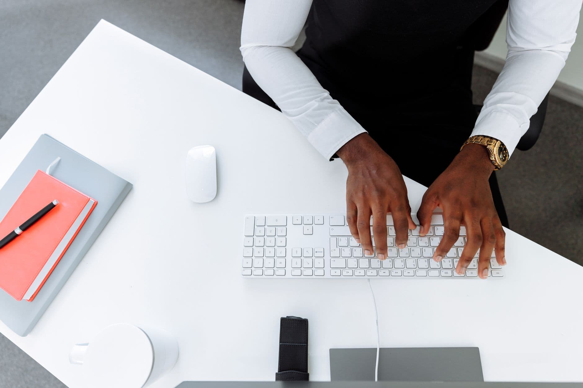 An overhead view of hands typing on a keyboard at a white desk