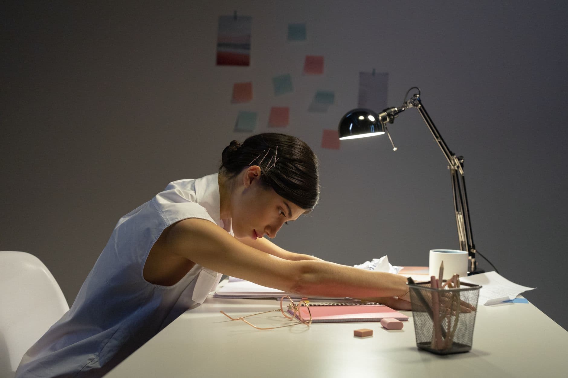 A tired person resting at a desk in a dimly lit office