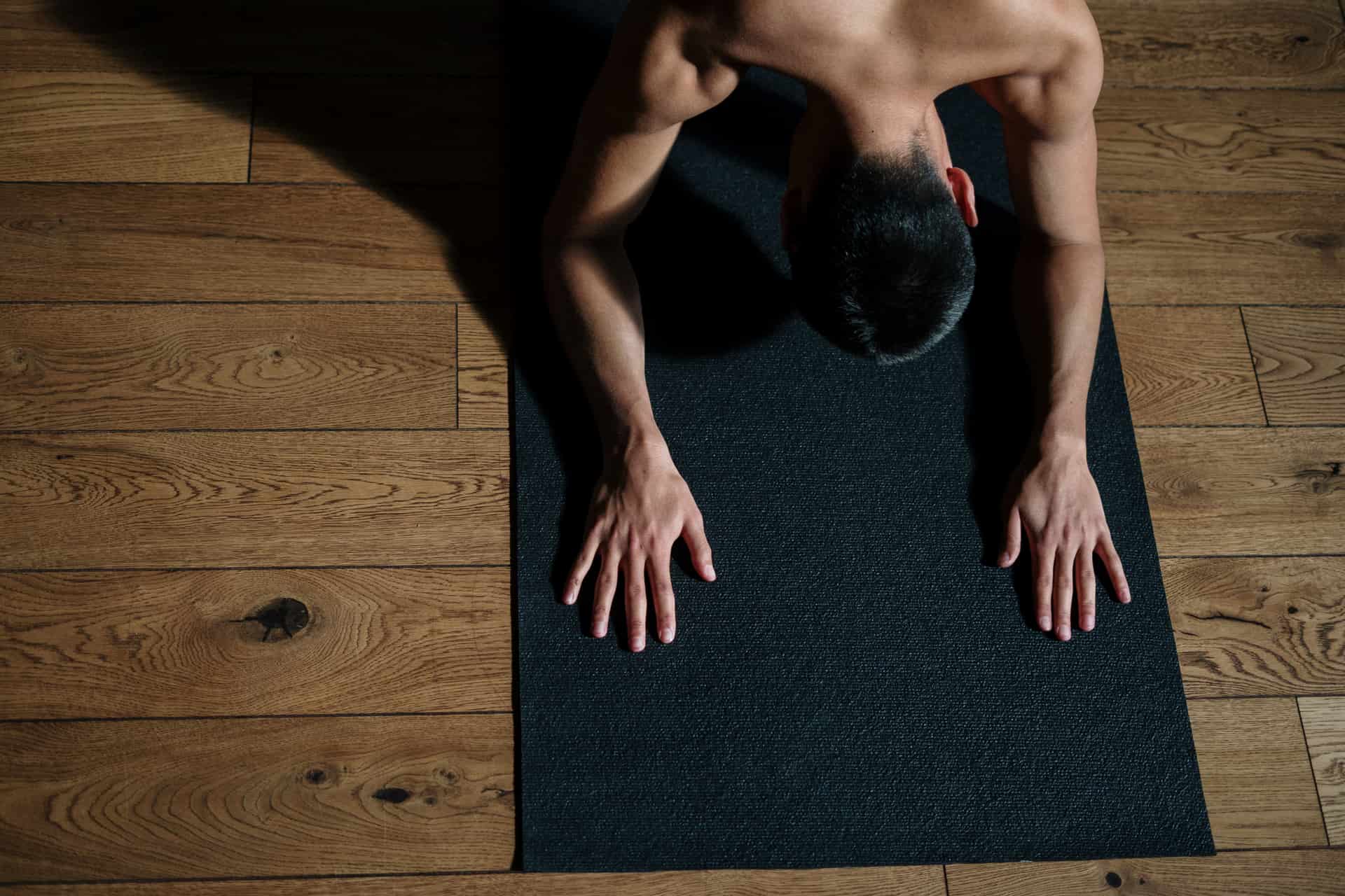 A contoured anti-fatigue standing mat on a wooden floor in front of a standing desk