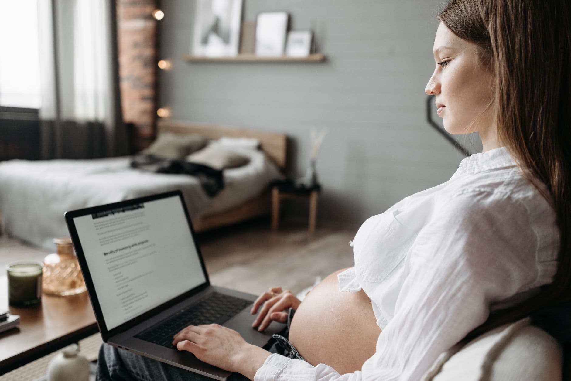 A pregnant woman working on a laptop at a desk, seen from the side