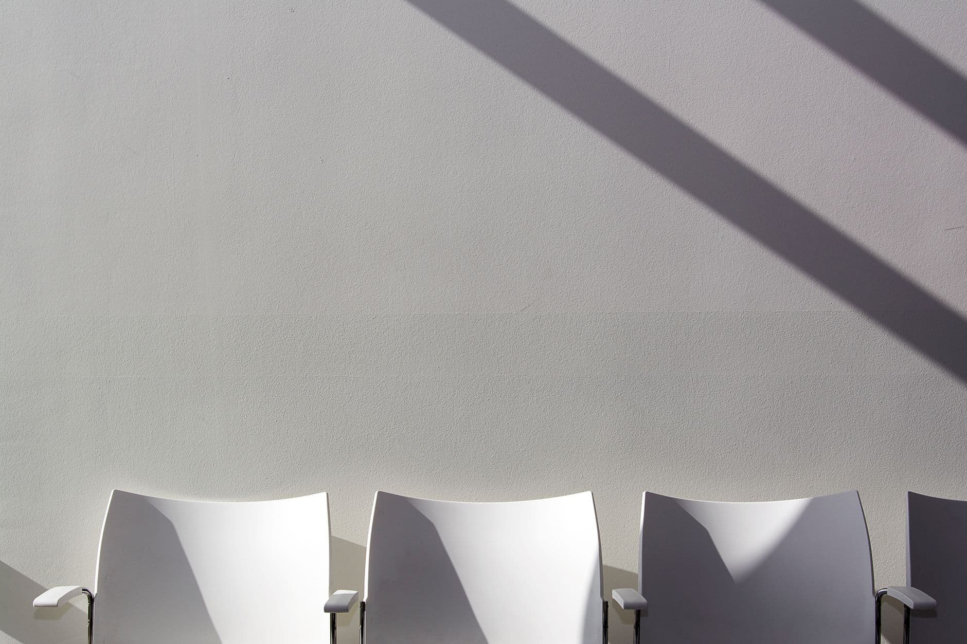 Three white chairs casting long shadows against a plain wall